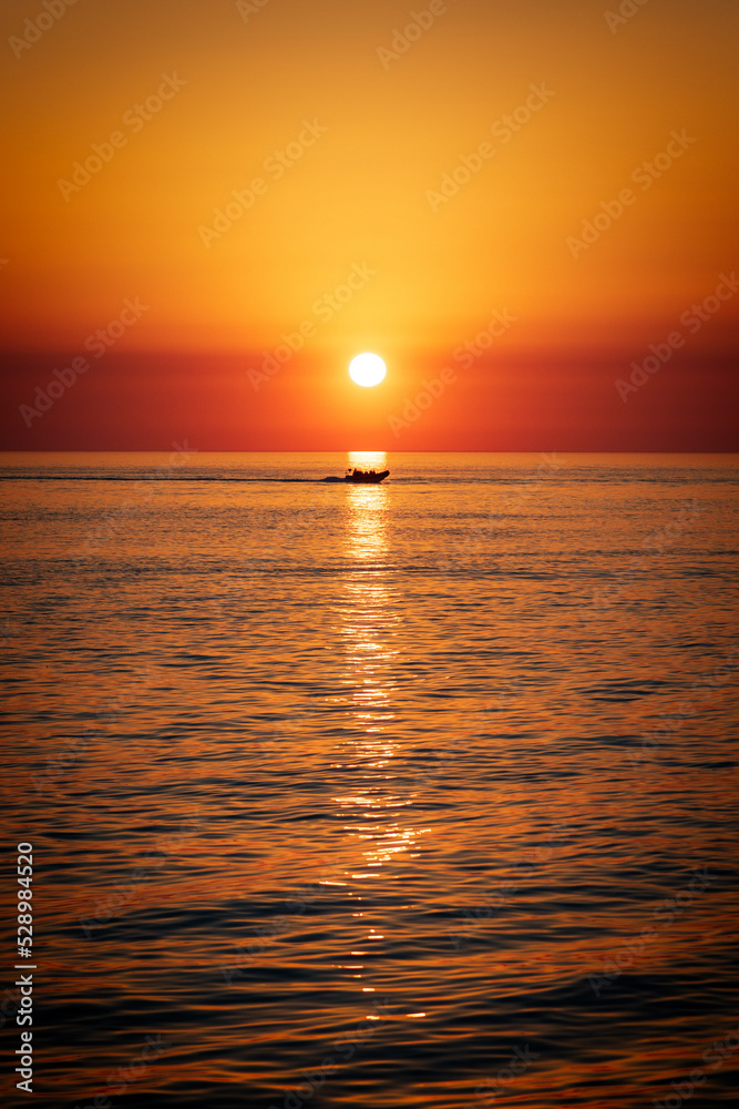 Obraz premium sunset over the sea with rigged inflatable boat RIB crossing through the sunlight reflection