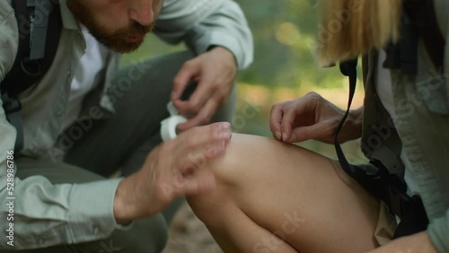 Emergency medical help. Close up shot of caring man putting adhesive tape on female knee, woman falled down in forest
