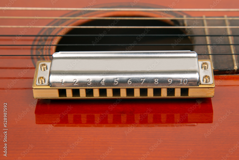 The harmonica rests on the body of a classical guitar. Classical musical wind instrument. The harmonica rests on the body of a classical guitar. Classical musical wind instrument.