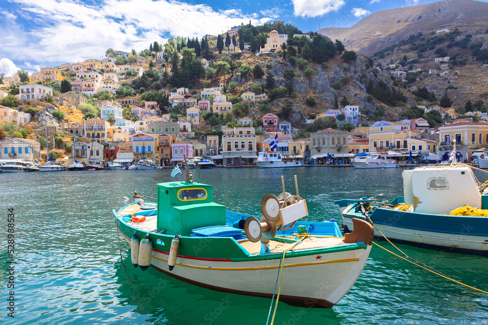 Panoramic view, aerial skyline of small haven of Symi island. Village with tiny beach, moored boats and colorful houses located on rock. Tops of mountains on Rhodes coast, Greece