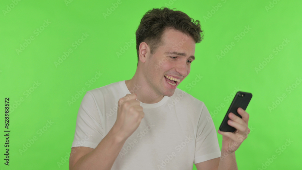 Young Man Celebrating on Smartphone on Green Background Young Man Celebrating on Smartphone on Green Background