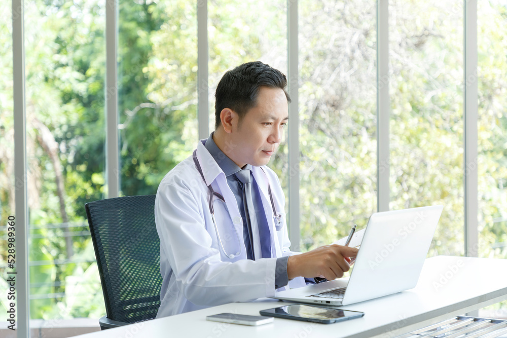 Portrait of asian senior doctor sitting in medical office while using laptop computer and checking time of appointment. Portrait of asian senior doctor sitting in medical office while using laptop computer and checking time of appointment.