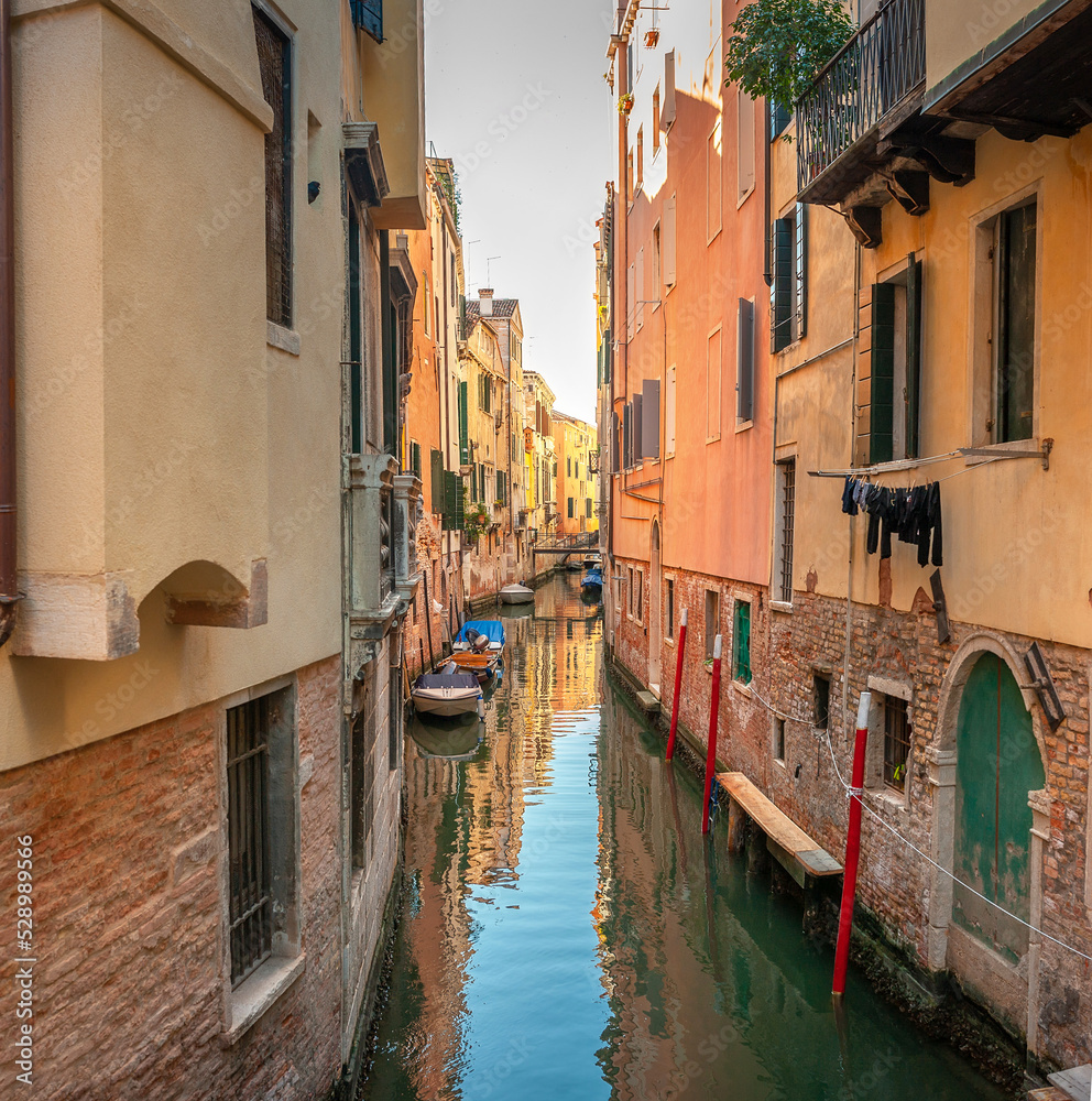 View on the narrow cozy streets of the canals with parked boats in Venice, Italy. Architecture and landmark of Venice.