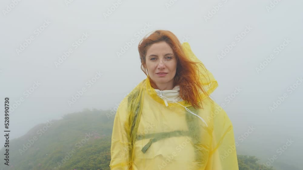 Portrait of a woman in a foggy weather looking into the camera hair and coat blowing in the wind. Mountaineer woman taking another mount peak. Goal achieving idea.