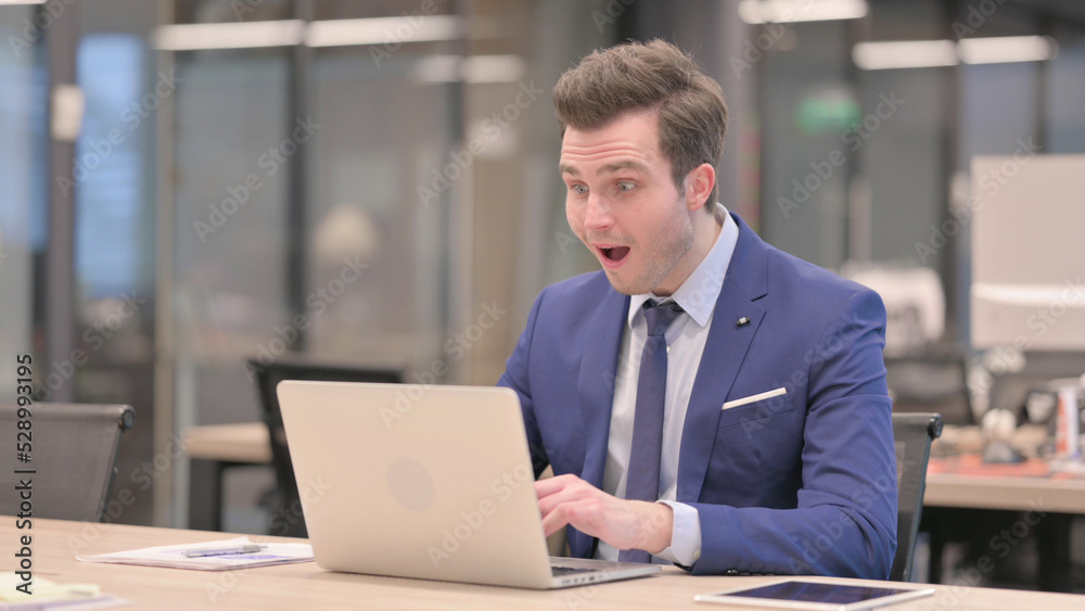 Businessman Celebrating Success while using Laptop in Office