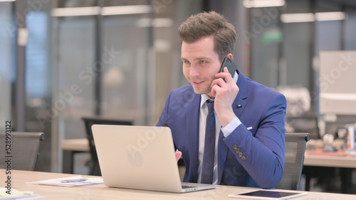 Businessman Talking on Phone while using Laptop in Office