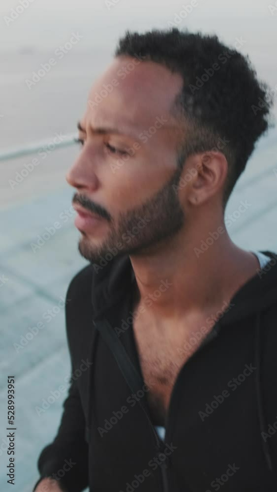 VERTICAL VIDEO: Close up, young bearded male athlete runs along the promenade VERTICAL VIDEO: Close up, young bearded male athlete runs along the promenade
