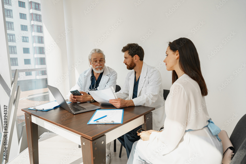 Two doctors in white uniform consult female patient at meeting in private clinic. High quality photo Two doctors in white uniform consult female patient at meeting in private clinic. High quality photo