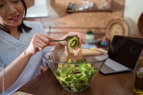 Asian female adding kiwi to salad photo