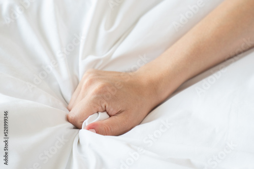 Hand of woman with neat manicure touches and grabs clean white sheet put on bed. Female tourist enjoys morning in comfortable hotel room closeup