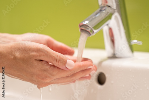 Woman with nice manicure washes hands over sink turning on water. Tourist takes care of herself washing hands from bacteria and viruses closeup photo