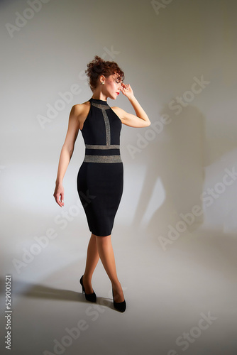Portrait of beautiful slim young woman with short brunette hair in black dress in studio with white background. Girl model posing during photo shoot