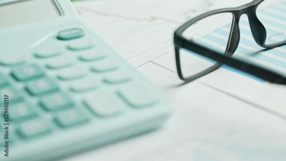 Documents with calculator. Printed stock graphs and charts. Analyzing financial data report and business concept. Profit and tables on work desk Documents with calculator. Printed stock graphs and charts. Analyzing financial data report and business concept. Profit and tables on work desk