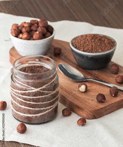 Homemade cocoa cream with hazelnuts in a jar on a tableboard. Sweet and healthy food. photo