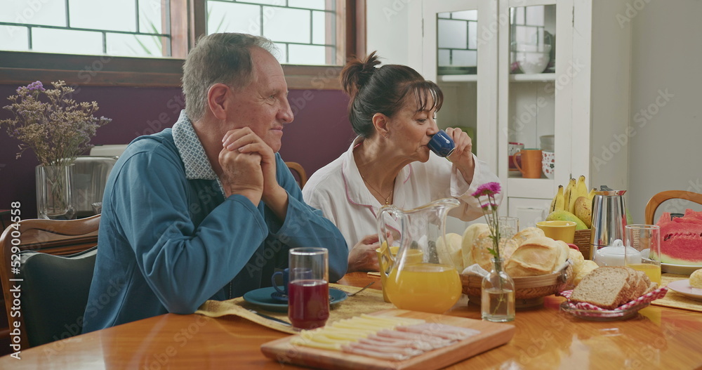 Happy couple having breakfast with teenage daughter sitting at kitchen table. The father is talking and the mother is serving juice to the daughter