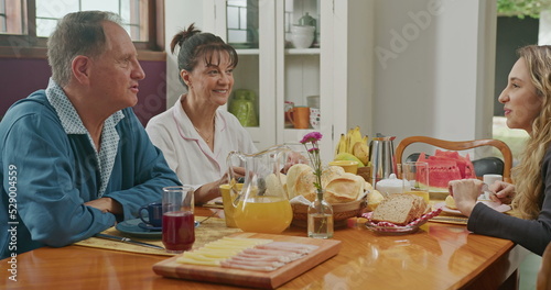 Happy couple having breakfast with teenage daughter sitting at kitchen table. The father is talking and the mother is serving juice to the daughter