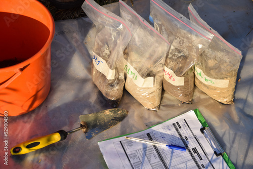 Slika na platnu High angle view of sample bags with soil samples, garden tool, information sheet form outdoors