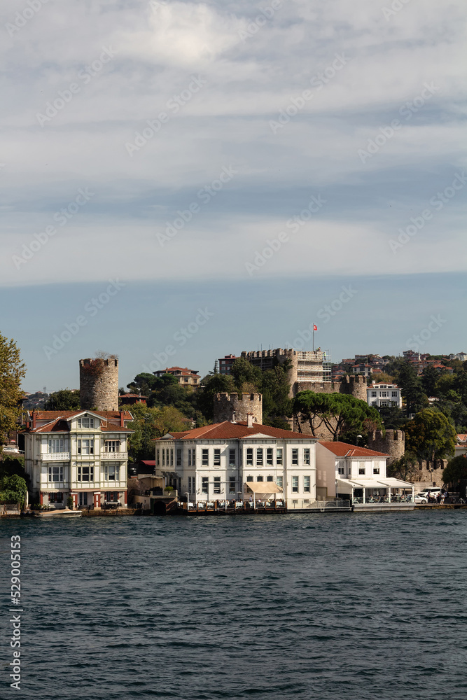 Obraz premium View of historical, traditional mansions and old Anatolian fortress by Bosphorus in Anadolu Hisari area of Asian side of Istanbul. It is a sunny summer day. Beautiful travel scene.