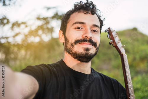 Young smiling Latin guitarist takes a selfie with his cell phone