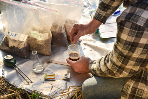 Male agronomy specialist testing soil sample outdoors, using laboratory equipment, performing soil certification at agricultural grain field sunrise. Environment research, soil certification