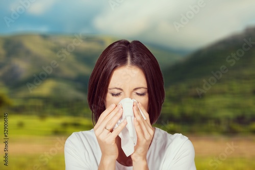 Young pretty woman blowing nose in front of blooming tree. Spring allergy concept. Sick people allergy or virus influenca concept. photo