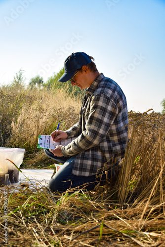 Male agronomist preparing soil samples for laboratory analysis, writing in information sheet outdoors at sunrise. Man farmer taking notes in form, working at field. Soil certification