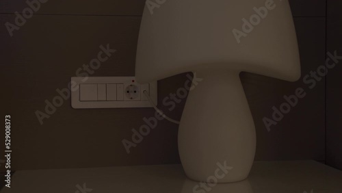 Hand of woman pushes button on white switch to turn off light in hotel room. Guest switches off bright lamp standing on bedside table close view photo