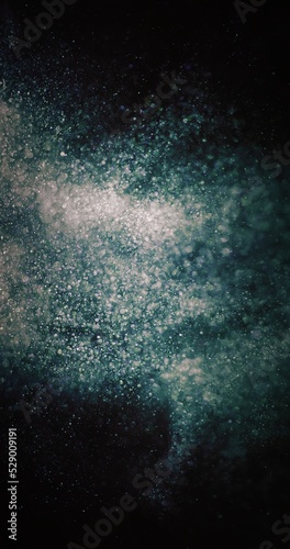 Particles background. Dust splash. Cosmic collision. Defocused green blue white bubbles burst on dark night black abstract wallpaper.
