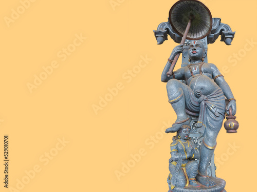 Vamana or Vamanadeva - Hindu God, Brahmin boy, dwarf with umbrella. Giant Indian temple statue. Isolated on a beige background. Happy Vamana Dvadasi. photo