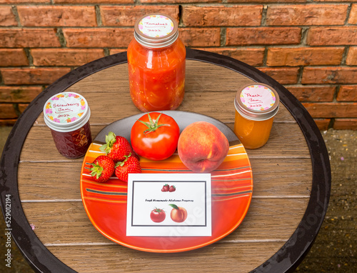 Assortment of homemade tomato, strawberry, and peach preserves from a local farmer in Clanton, Alabama and displayed on a table and saucer. Labels created by Photog. photo