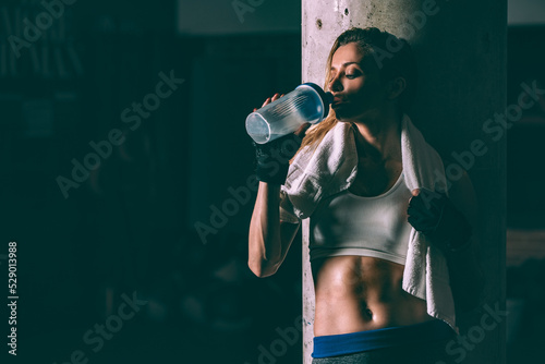 Fit blonde tired woman resting and drinking after training working out in Gym photo