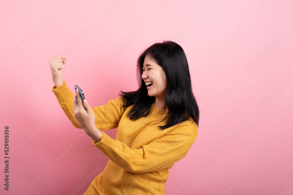 Portrait of a cheerful, happy and cute brown-haired girl using a smartphone device, posting an app like an isolated reaction on a yellow background.