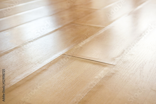Swollen laminate flooring from flood or water damage, perspective view. Close up of light beige buckling laminate boards with bent edge pieces. Floor damage texture. Selective focus in center.