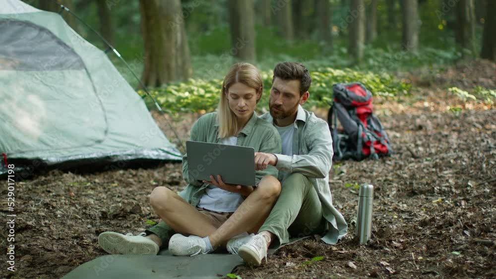 Happy middle aged spouses resting at camping and web surfing online on laptop, bonding near tent, free space Happy middle aged spouses resting at camping and web surfing online on laptop, bonding near tent, free space