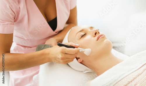 Beautician cosmetologist applies cosmetic product gel peeling mask with spatula, professional procedure in a beauty clinic salon for client. Skincare and cosmetology spa concept.	