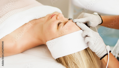 Beautician cosmetologist makes a procedure on the face with microcurrent therapy gloves. Hardware cosmetology in clinic salon for client.	 photo