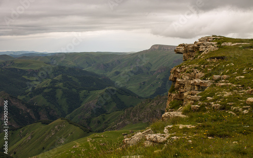 Panoramic view of the canyon with green hills blurred by misty haze to the horizon and steep high cliffs of the Bermamyt plateau in Karachay-Cherkessia