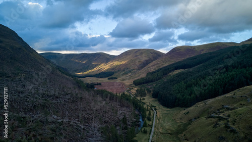 An aerial view of Glen Doll - mountains, pine forest on slopes and a road under evening sky photo