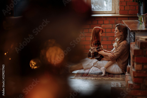 Little girl in a dress sits by the Christmas tree