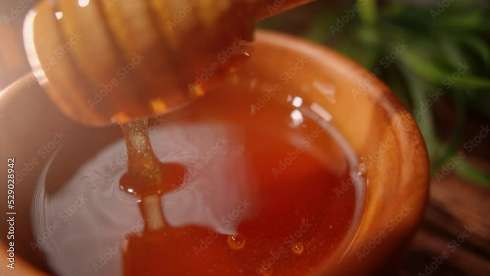 A person is dipping wooden spoon in honey. Golden fresh honey is pouring from stick. Organic beekeeping. Concept of healthy organic food and sweet meals.