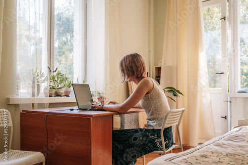 Photography Young woman sitting by window, working, studying or surfing with laptop