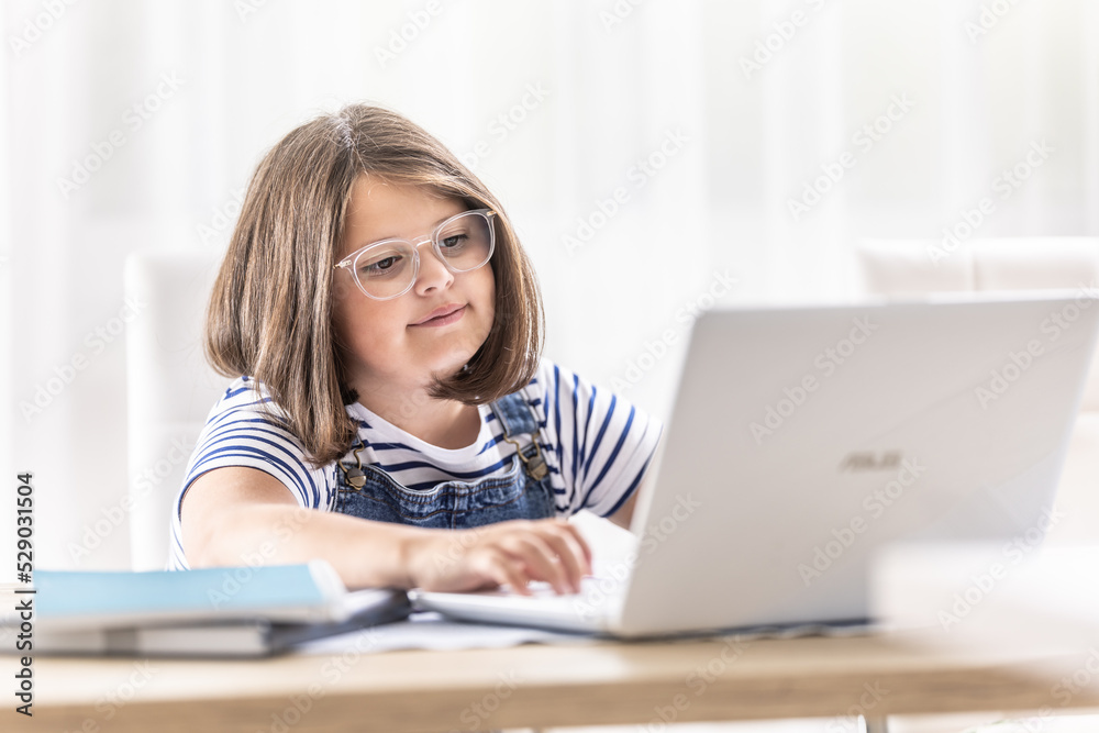 Round-faced girl wearing glasses sits behind a laptop looking into it Round-faced girl wearing glasses sits behind a laptop looking into it