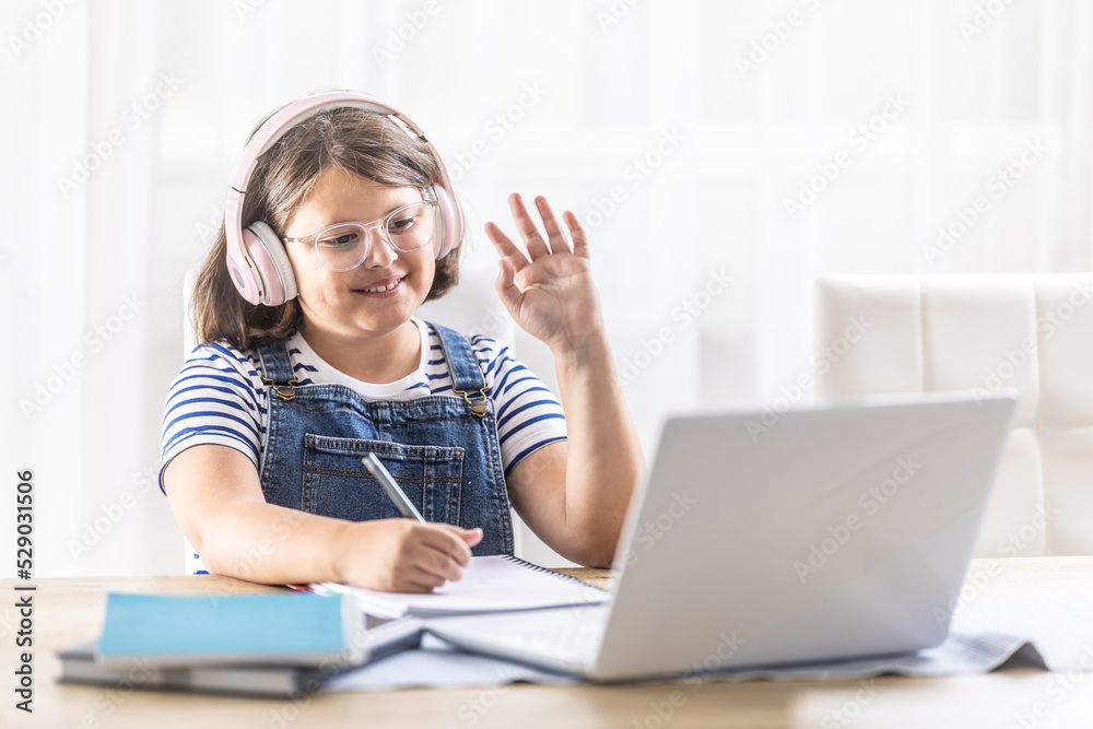 Chubby schoolgirl in glasses and headphones waves at her schoolmates on the computer during distant studies Chubby schoolgirl in glasses and headphones waves at her schoolmates on the computer during distant studies