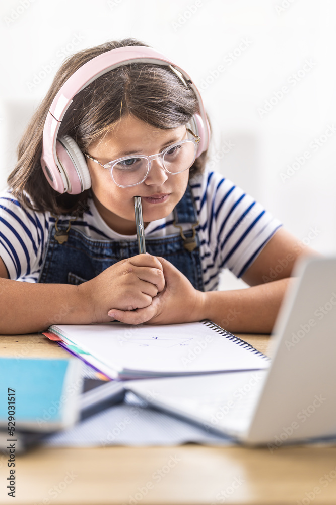 Hard-studying girl in glasses wears headphones and chews on pencil in her hand looking into the pc Hard-studying girl in glasses wears headphones and chews on pencil in her hand looking into the pc