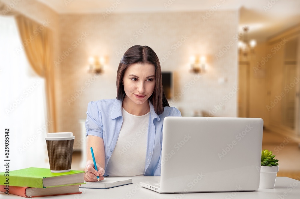 Cheerful college student attending virtual class, writing notes, watching webinar on Internet, studying online.