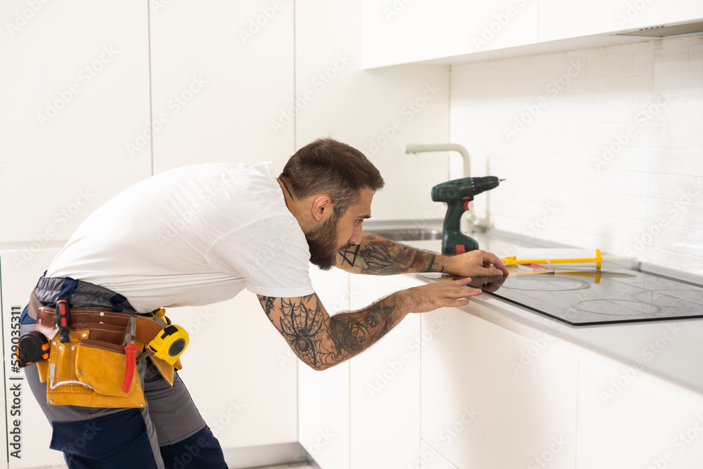 craftsman installs hob in kitchen. Household Appliance Installation Services Concept craftsman installs hob in kitchen. Household Appliance Installation Services Concept