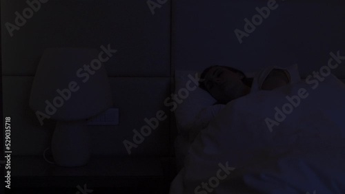 Woman gets in bed switching off bright lamp standing on bedside table. Female guest turns off light in hotel room before falling asleep closeup photo