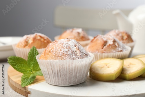 Tasty muffins served with mint and banana on board, closeup