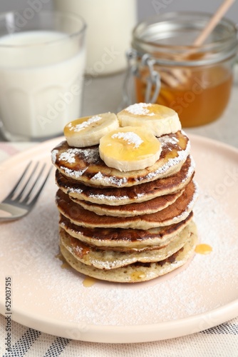 Plate of banana pancakes with honey and powdered sugar served on table, closeup