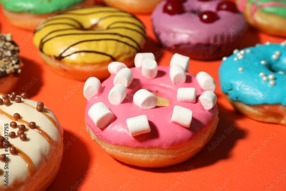 Sweet tasty glazed donuts on coral background, closeup